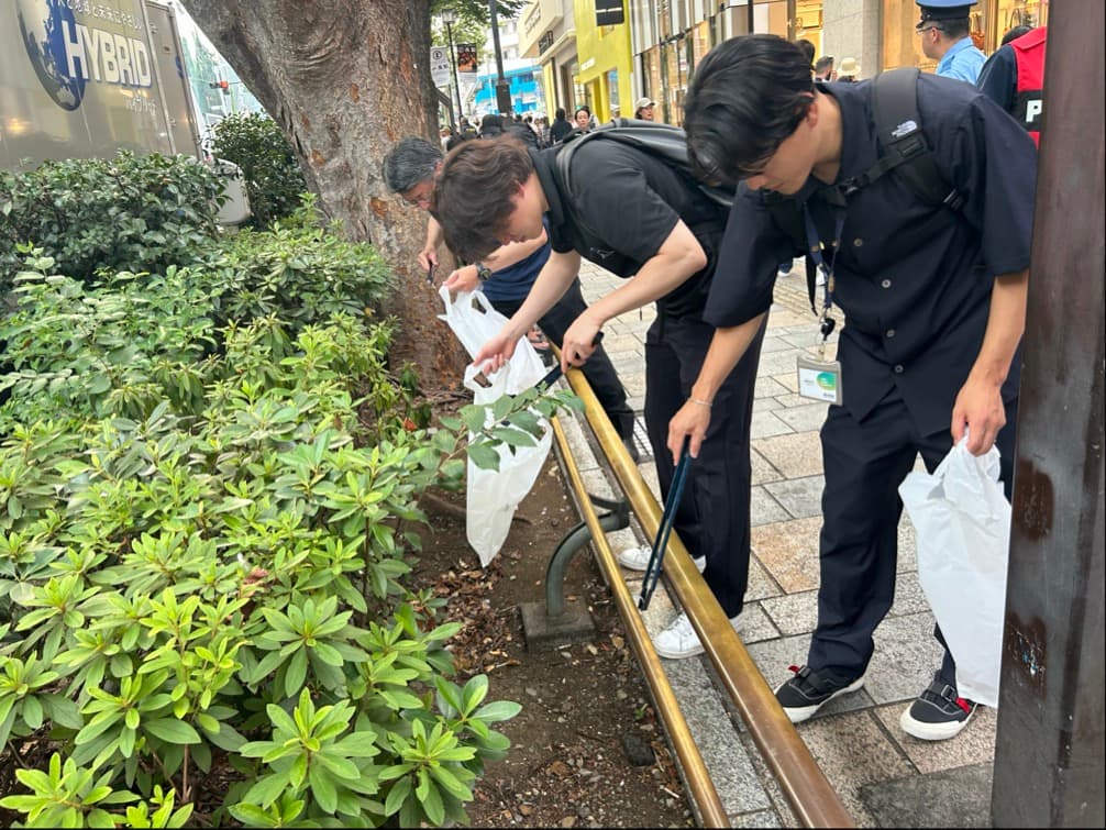 道路沿いの植え込みでゴミを拾うボランティア参加者